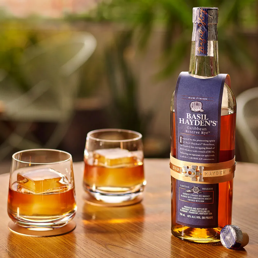 A bottle of Basil Hayden Caribbean Reserve Rye and two glasses filled with the bourbon